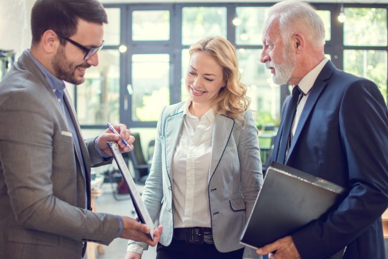 A businessman showing a document on a clipboard to his business colleagues in the office.