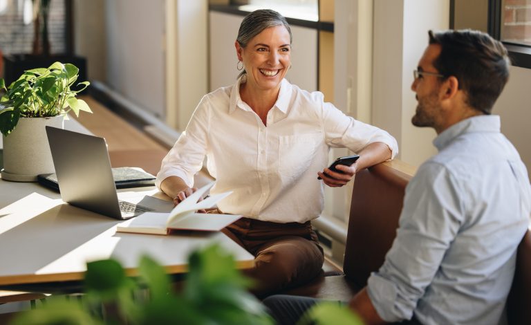 Businesswoman sitting at desk talking to a coworker.