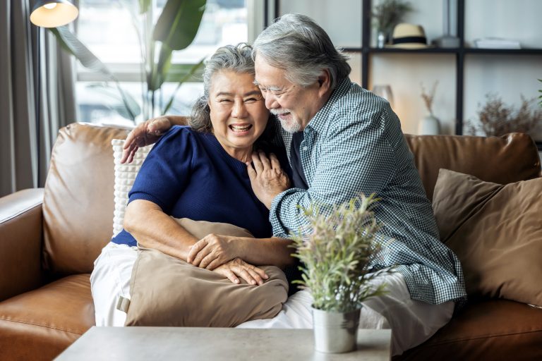 Retired couple sitting on a couch at home and laughing.