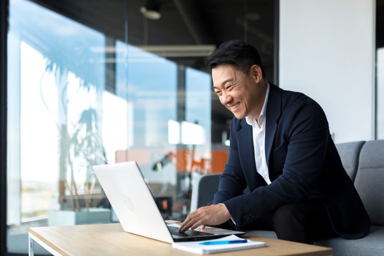 Asian businessman smiling while working on his laptop.