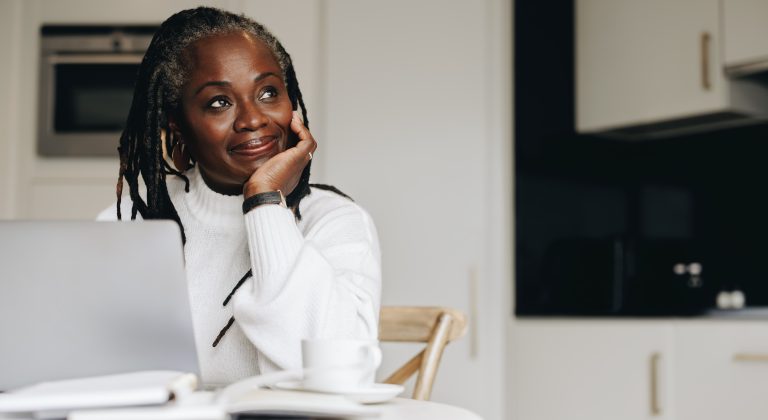 Mature businesswoman looking away thoughtfully while working on a laptop at home.